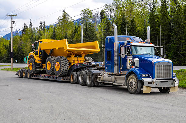 Big truck with a low platform trailer carrying a tipper truck on a public parking area of a truck stop